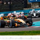 Im Vordergrund ein Formel-1-Auto bei einem Rennen, umgeben von anderen Fahrzeugen. Rennstrecke mit Zuschauern im Hintergrund.