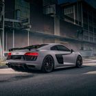 Auf der Rückseite eines Sportwagens ist das Audi-Logo zu sehen. Der Wagen steht vor einem Industriegebäude.