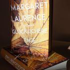 Text: "Margaret Laurence. Roman. Glücklichere Tage. Mit einem Nachwort von Helene Bukowski. Eisele."  
Ein Buch mit einem Herbstlaub-Covermotiv.