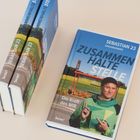 "SEBASTIAN 23", "ZUSAMMEN HALTE STELLE", "Die Kraft des WIR". Zwei Bücher gestapelt, eins liegt flach.