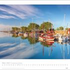 März 2027, Schleswig-Holstein. Hafen mit Segelbooten, ruhiges Wasser, klare Spiegelung der Umgebung, blauer Himmel, Bäume.