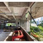 Ein Loft mit Betonwänden, großen Fenstern, rotem Ledersofa, Bücherregal, Holztisch und Blick auf Grünflächen und Stadt.