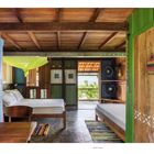 Text: "A CASA PROTEGE O SONHAD"  
Beschreibung: Ein gemütliches Zimmer mit Holzinrichtung, bunten Teppichen, einem Himmelbett und Blick auf die Natur.