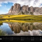Dolomitenkalender im März, Spiegelung von Bergen im See, grüne Wiesen, blauer Himmel, „Lastoi de Formin“.