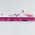 Pinkes Regal mit verschiedenen Gläsern, Schalen und Flaschen, gefüllt mit lila oder rosa Flüssigkeiten.