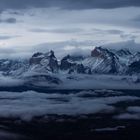 Schneebedeckte Bergkette umgeben von dichten Wolken und Nebel, mit einem düsteren Himmel im Hintergrund.