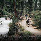 Kalender mit März-Daten unten. Zwei Radfahrer fahren auf einem Waldweg neben einem fließenden Bach.