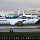 „Lufthansa“ auf einem Flugzeug. Kalender unten zeigt Zahlen und Wochentage. Hinter dem Flugzeug Gebäude und andere Jets.