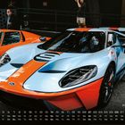 Ford GT 40. Kalender: Mo-Su, 1-31. Hellblauer Sportwagen mit orangenen Streifen, steht auf einem Parkplatz.