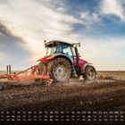 Kalender mit Märztagen unten. Ein roter Traktor pflügt ein Feld, Himmel mit Wolken im Hintergrund.