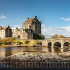 "Eilean Donan Castle" und Monatskalender im Vordergrund. Eine historische Burg auf einer kleinen Insel mit Brücke, umgeben von Wasser.