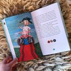 Seite 51: Ein Schaf und ein Schwein auf roter Rutsche, umgeben von Wiese und blauem Himmel. Hand hält das Buch auf hellem Teppich.