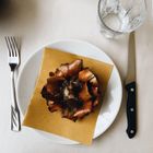 Kein Text vorhanden. Auf einem Teller liegt eine kunstvoll arrangierte braune Blume, daneben Glas, Gabel, Messer.