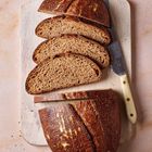 Fünf Scheiben Brot auf Holzbrett, daneben Messer mit hellem Griff, Oberfläche krustig braun.