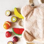 Spielzeugobst aus Holz: Kiwi, Banane, Orange, Erdbeere, Apfel, Melone neben einem plüschigen Rucksack mit Ohren.
