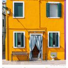 Kalender mit Datum 28. Juni bis 4. Juli 2027. Gelbes Haus mit grünen Fensterläden und gestreiften Vorhängen.