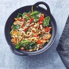 Ein schwarzer Teller enthält eine bunte Mischung aus Nudeln, Spinat, Paprika, Pilzen und Cashewnüssen.