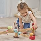 Ein Mädchen spielt fröhlich mit einer Holzmurmelbahn im Kinderzimmer. Sie trägt ein weißes Oberteil und blaue Jeans.