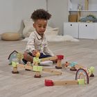 Ein Kind spielt auf dem Boden mit einer Holz-Murmelbahn im Spielzimmer. Im Hintergrund sind Regale mit Spielzeug.