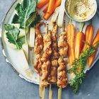 Eine Platte mit gegrillten Hähnchenspießen, frischen Möhren, Kohlrabi, Blättern und einer Sesam-Dip-Sauce.