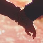 Zwei Hände halten sich vor einem warmen, verschwommenen Hintergrund. Illustration einer liebevollen Geste.