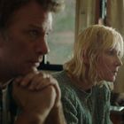 Zwei Personen in einem Raum, konzentriert und nachdenklich, sitzen nebeneinander. Hintergrund zeigt Vorhänge und ein Fenster.