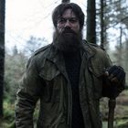 Es gibt keine Texte. Ein bärtiger Mann mit grünem Parka und Handschuh im Wald. Er hält einen Stock.