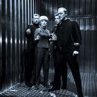 Vier Personen in futuristischer Kleidung halten Phaser in einem metallischen Raum.