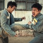 Auf zwei Uniformen sind gelbe Schilder mit Nummern. Zwei Männer kämpfen heftig, einer tritt den anderen gegen die Brust.