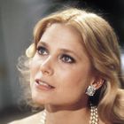 Keine sichtbaren Texte. Eine Frau mit blonden Haaren, Perlenkette und eleganten Ohrringen schaut nach oben.