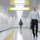 "Exit 8" auf einem gelben Schild in einem hellen Korridor. Eine Person geht weg, eine kommt entgegen.