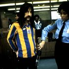 Ein Mann im gestreiften Trikot wird von einer Sicherheitsfrau mit einem Metalldetektor abgesucht.