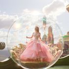 Eine Frau im rosa Kleid und Krone steht in einer schwebenden Seifenblase. Im Hintergrund sind fantasievolle Gebäude.