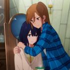 Zwei Personen in einem Raum voller Teegeschirr. Eine umarmt die andere tröstend; beide wirken nachdenklich.