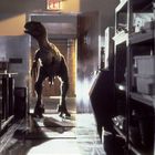Das Wort "EXIT" ist über einer Tür zu sehen. Ein Dinosaurier, ein Velociraptor wahrscheinlich, betritt einen hellen Raum.