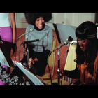 Eine Gruppe fröhlicher Menschen sitzt am Mikrofon. Sie lachen, während sie gemeinsam Musik machen.