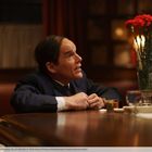 Ein Mann sitzt an einem Tisch, neben ihm steht eine Flasche mit dem Etikett "Old Forester" und eine Vase mit roten Nelken.