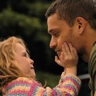 Ein Kind berührt das Gesicht eines Mannes liebevoll, während sie sich in die Augen schauen. Im Hintergrund Natur.