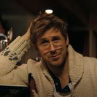 Text auf einer Flasche: "Bud Light". Ein Mann mit Brille und Wollpullover lächelt an einer Bar.