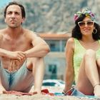 Ich kann den Text im Bild nicht erkennen. Ein Mann und eine Frau sitzen am Strand, sie trägt Sonnenbrille und Kopftuch.