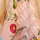 Text: "Hier blüht das Leben". Rosa Hintergrund mit bunten Blumenmotiven und Holzutensilien.
