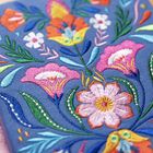 Eine bunte Stickerei mit Blumenmotiven auf blauem Stoff. Lebhafte Farben wie Pink, Orange und Grün prägen das Muster.