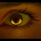 Ein Auge in Nahaufnahme, die Iris leuchtet feurig, umgeben von einer dunklen Pupille und dichten Wimpern.