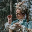 Person in historischer Kleidung mit aufwendigem Kopfschmuck im Wald, trägt eine goldene Vorrichtung auf der Nase.