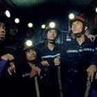 Sechs Bergleute in blauen Uniformen und Helmen mit Lampen blicken in einem engen Tunnel nach oben.