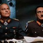 Zwei Männer in Militäruniformen mit Abzeichen und Eisernen Kreuzen sitzen an einem Tisch voller Dokumente.