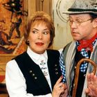 Eine Frau im Trachtenkleid spricht mit einem Mann in Lederhosen und Hut. Beide haben ernste Miene.