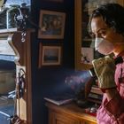 "CE EN 388 EN 420" auf Handschuh. Person mit Maske hält Taschenlampe, steht in rustikalem Raum mit Regalen und alter Einrichtung.