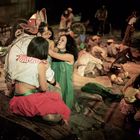 Es gibt keinen Text. Eine Gruppe von Menschen sitzt oder liegt zusammen, in bunter, traditioneller Kleidung.