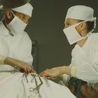 Chirurgen in OP-Kleidung arbeiten konzentriert über einem Patienten, umgeben von chirurgischen Instrumenten.